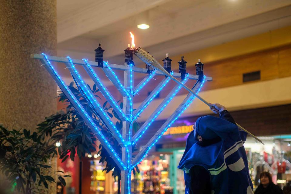A member of the "Roving Rabbis" lights the first candle of the menorah, known as the shamash or helper candle, Thursday at the Westgate Mall in Amarillo.