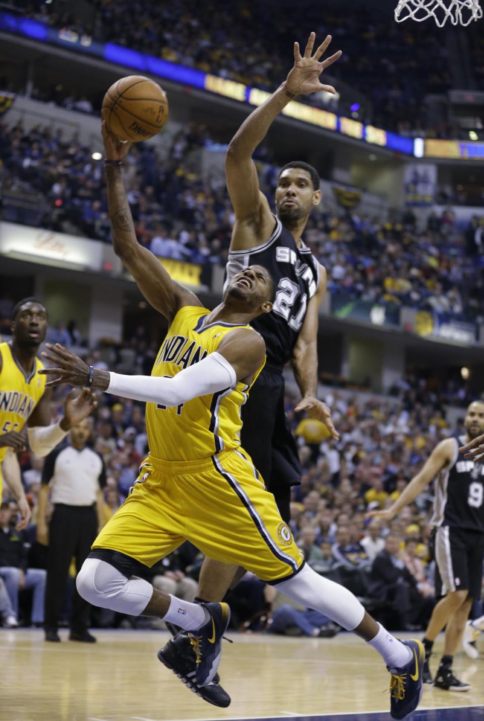 Indiana Pacers forward Paul George, left, is fouled from behind by San Antonio Spurs forward Tim Duncan in the first half of an NBA basketball game in Indianapolis, Monday, March 31, 2014. (AP Photo/Michael Conroy)