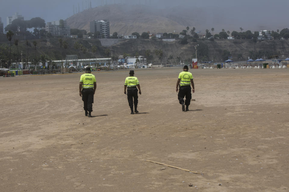 In this March 24, 2020 photo, policemen walk along an empty shore on the final days of the Southern Hemisphere summer to warn off would be swimmers as a precaution contain the spread of the new coronavirus, at Agua Dulce beach in Lima, Peru. (AP Photo/Rodrigo Abd)