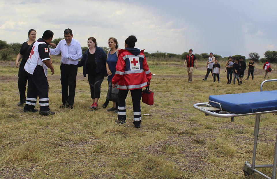 In this photo released by Red Cross Durango communications office, Red Cross workers attend airline passengers who survived a plane crash, as they walk away from the crash site in a field near the airport in Durango, Mexico, Tuesday, July 31, 2018. An Aeromexico jetliner crashed while taking off during a severe storm, smacking down in a field nearly intact then catching fire, and officials said it appeared everyone on board escaped the flames. (Red Cross Durango via AP)