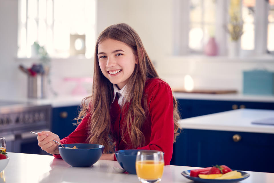 Portrait Of Smiling Teenage Girl Wearing School Uniform In Kitchen Eating Healthy Breakfast