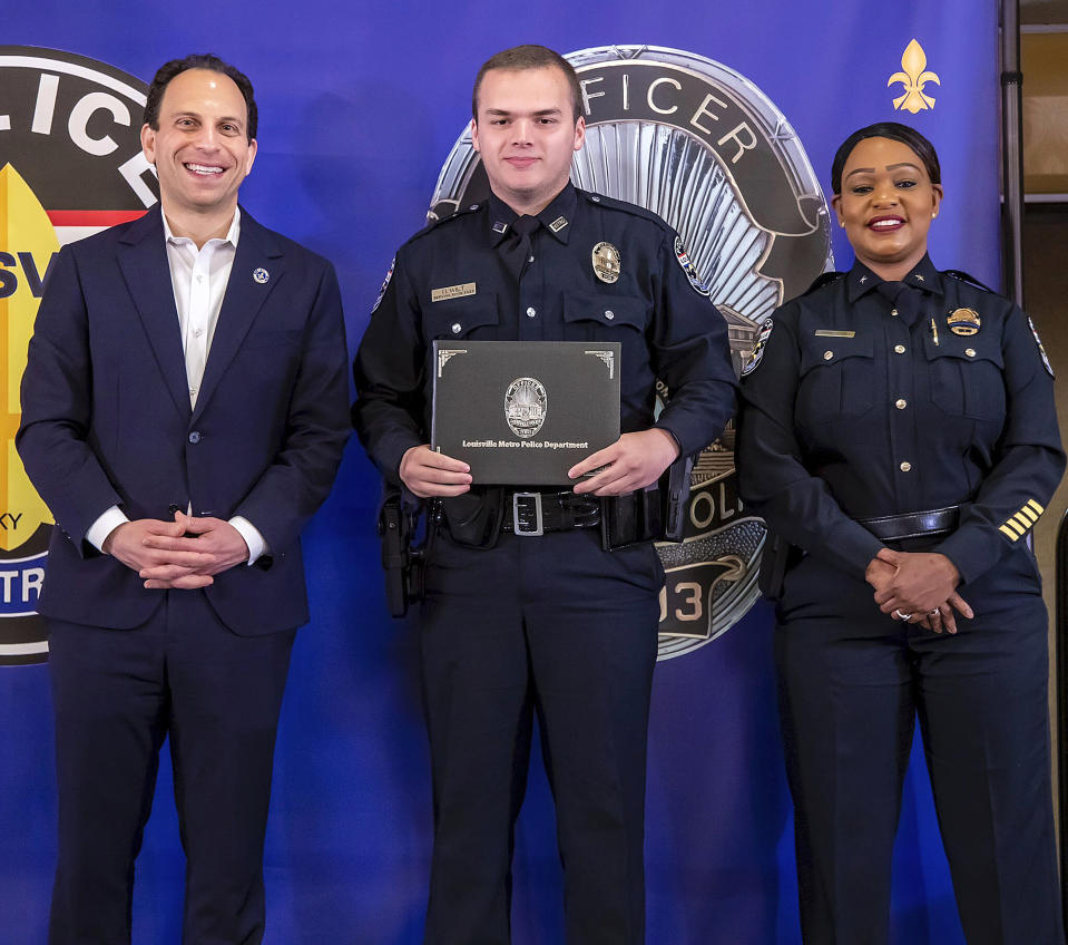 In this photo provided by the Louisville Metro Police Department, from left, Louisville Mayor Craig Greenberg, Officer Nickolas Wilt and Louisville Metro Interim Police Chief Jacquelyn Gwinn-Villaroel pose for a photo, in Louisville, Ky., March 31, 2023. Wilt was shot while responding to a call where a bank employee armed with a rifle opened fire at his workplace early Monday, April 10. (Louisville Metro Police Department via AP)
