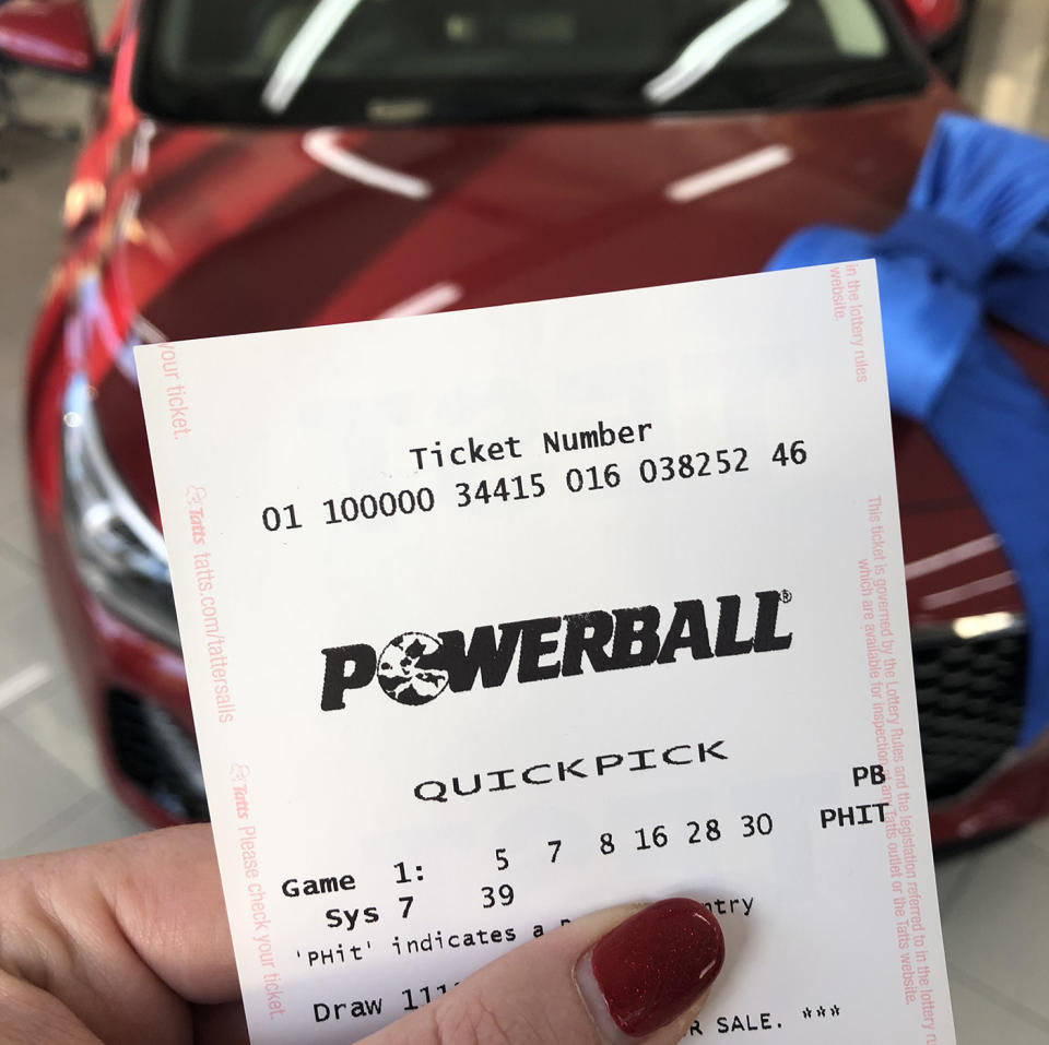 Powerball ticket held up in front of new car.