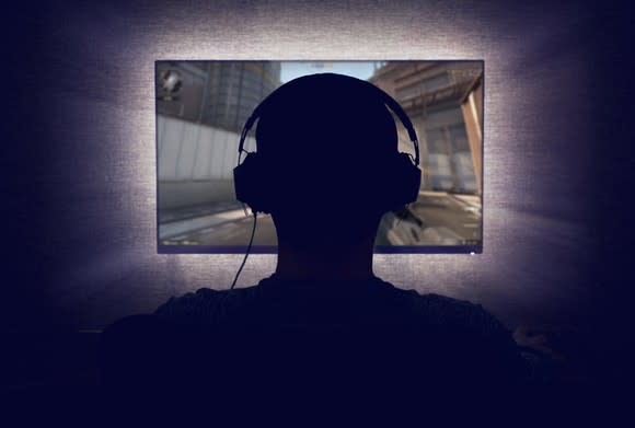 A person sitting in front of a monitor wearing headphones.