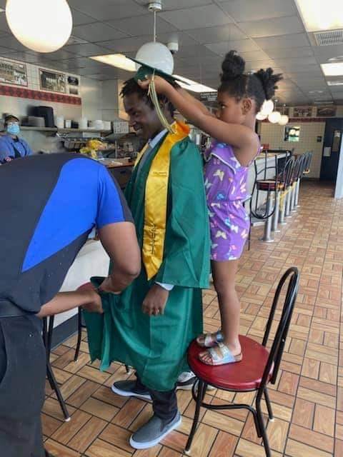 Waffle House manager Cedric Hampton helps one of his employees, Timothy Harrison, put on his cap and gown. Harrison showed up to work on the day of his high school graduation ceremony, but his Waffle House co-workers worked together to make sure he made it to the ceremony.