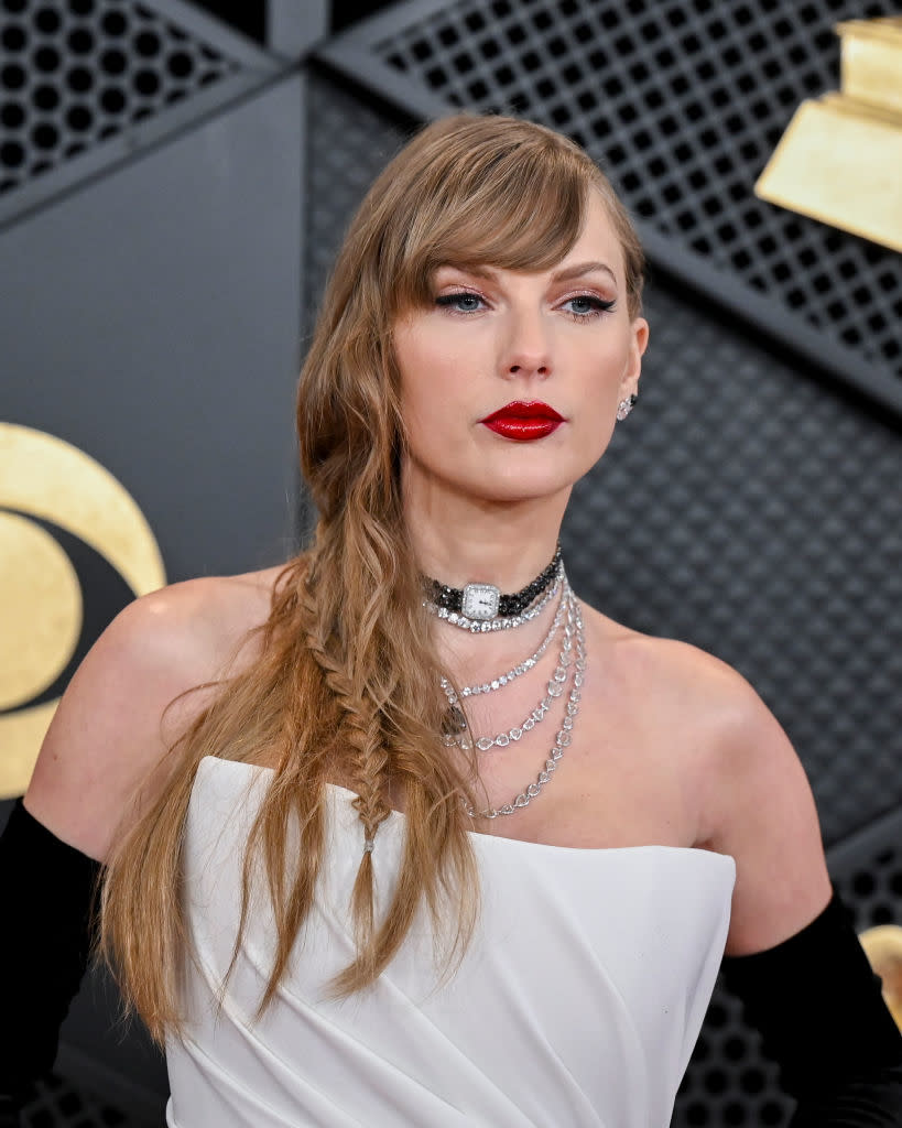 Taylor Swift wearing a white off-shoulder dress with layered necklaces, posing at an event