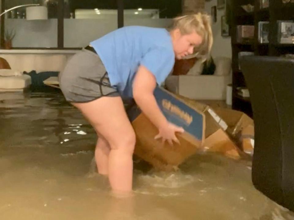 A woman picks up boxes in a flooded apartment in Dallas, Texas, U.S. August 22, 2022, in this picture taken from a social media video.