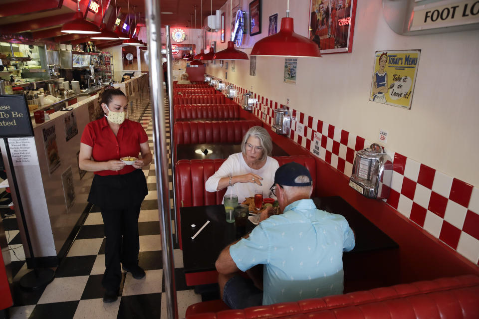 Lynn Tanner, center, and her husband Ryan, bottom right, are served lunch at Busy Bee Cafe Thursday, May 21, 2020, in Ventura, Calif. Much of the country remains unlikely to venture out to bars, restaurants, theaters or gyms anytime soon, despite state and local officials increasingly allowing businesses to reopen. That's according to a new survey by The Associated Press-NORC Center for Public Affairs Research. (AP Photo/Marcio Jose Sanchez)