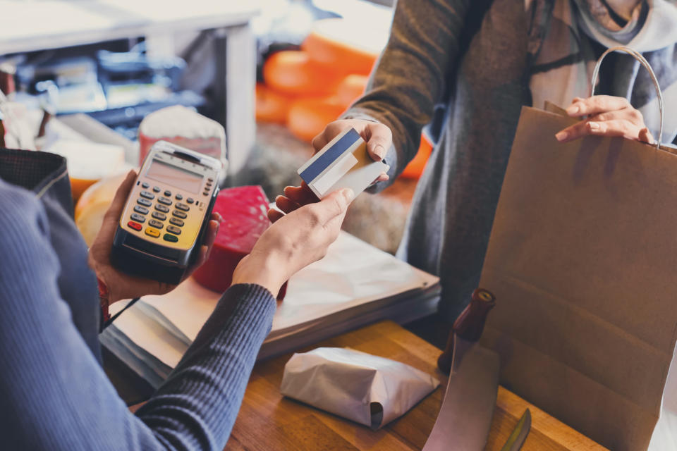 Customer hands merchant a credit card over the counter at a retail store.