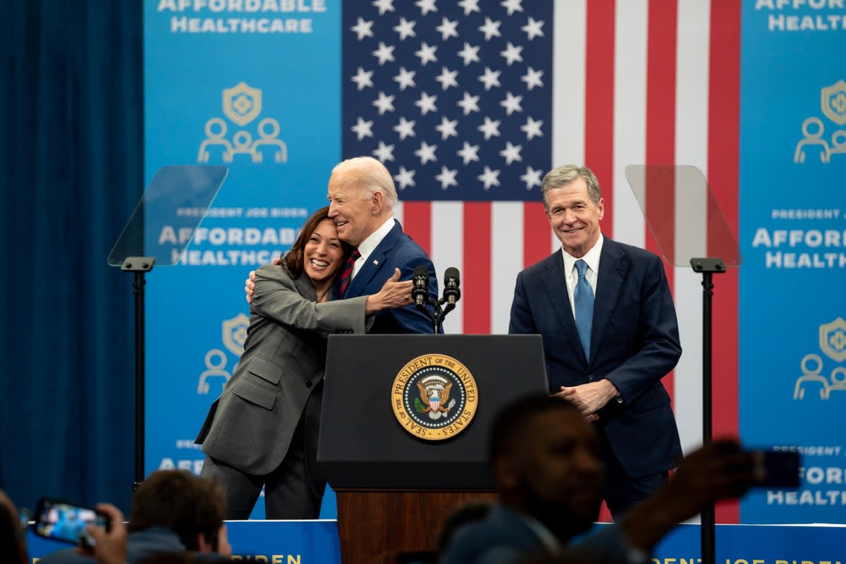 US President Joe Biden hugs Kamala Harris, the vice-president, as Roy Cooper, the governor of North Carolina, looks on during an event at the Chavis community centre on 26 March 2024 in Raleigh, North Carolina (Getty Images)