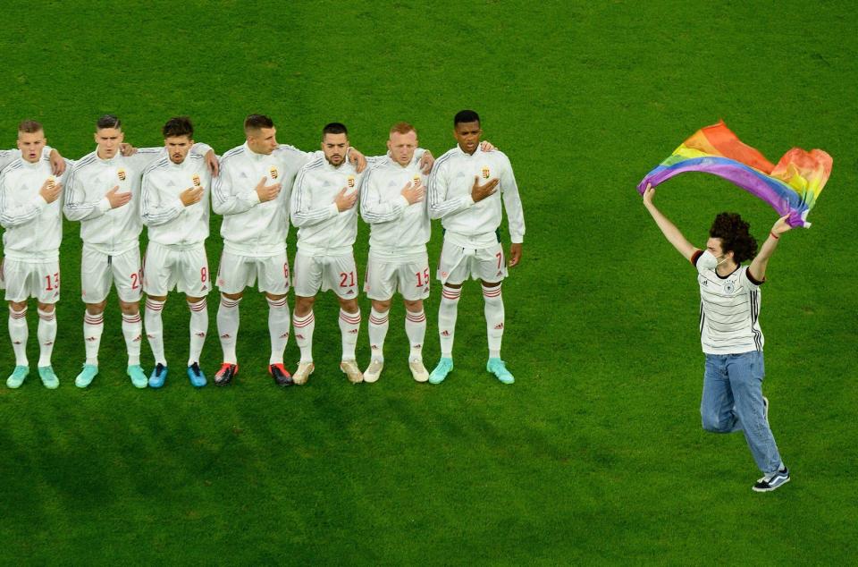 A fan runs on to the pitch waving a rainbow flag in front of Hungary's footballers