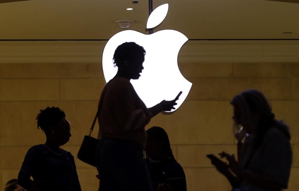 FILE PHOTO: Women uses an iPhone mobile device as she passes a lighted Apple logo at the Apple store at Grand Central Terminal in New York City, U.S., April 14, 2023. REUTERS/Mike Segar/File Photo