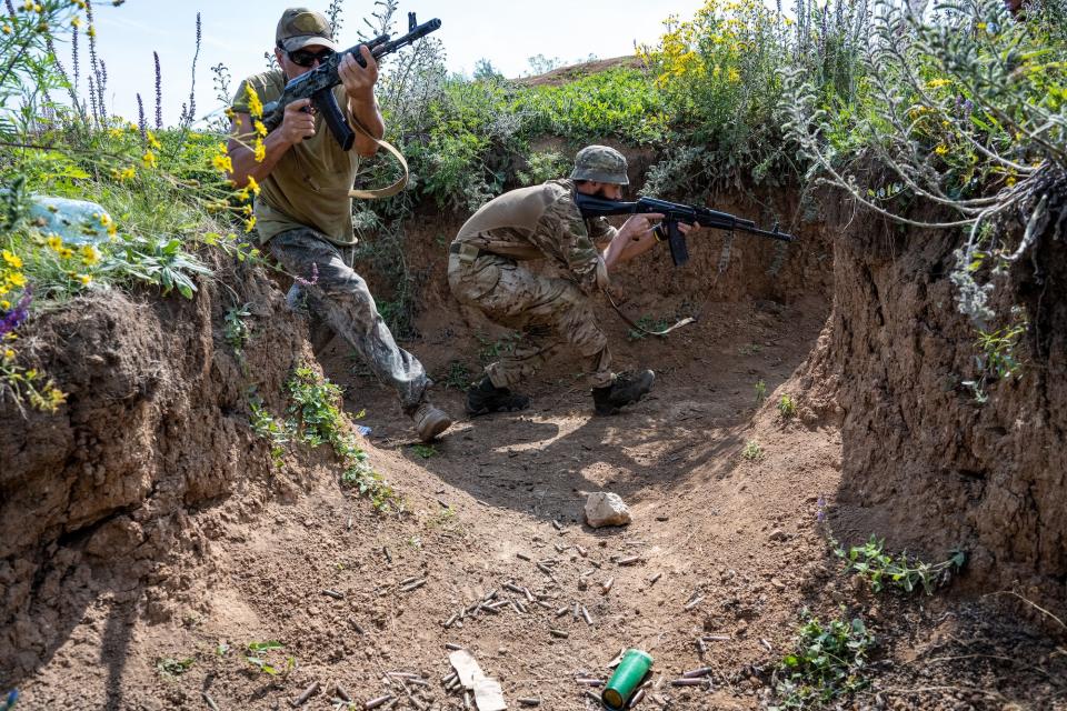 Two troops in a trench, holding guns.