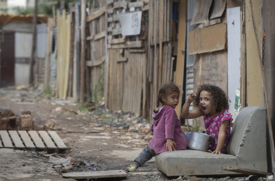 FILE - In this May 15, 2021, a girl eats from a pot as she eyes the camera in the Penha Brasil favela where families have started relocating during the coronavirus pandemic in Sao Paulo, Brazil. The shantytown's rapid rise reflects a resurgence in poverty after the government limited socioeconomic turmoil in 2020 with one of the world's most generous welfare programs. (AP Photo/Andre Penner, File)