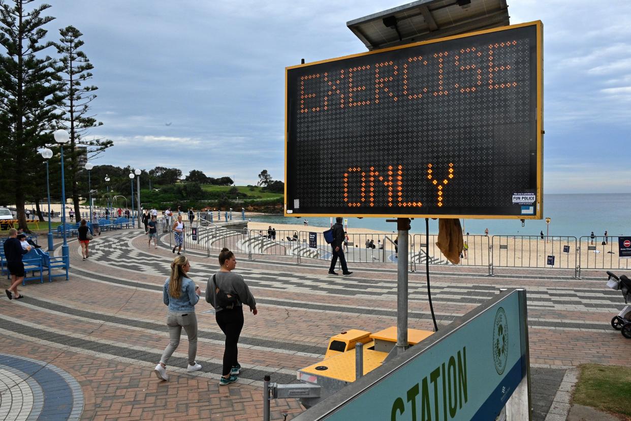 People walk past a sign reading "exercise only" at Coogee Beach in Sydney on April 20, 2020. - Authorities in Sydney reopened three beaches for walking, running, swimming or surfing only amid lockdown restrictions put in place due to the COVID-19 coronavirus outbreak. (Photo by Saeed KHAN / AFP) (Photo by SAEED KHAN/AFP via Getty Images)