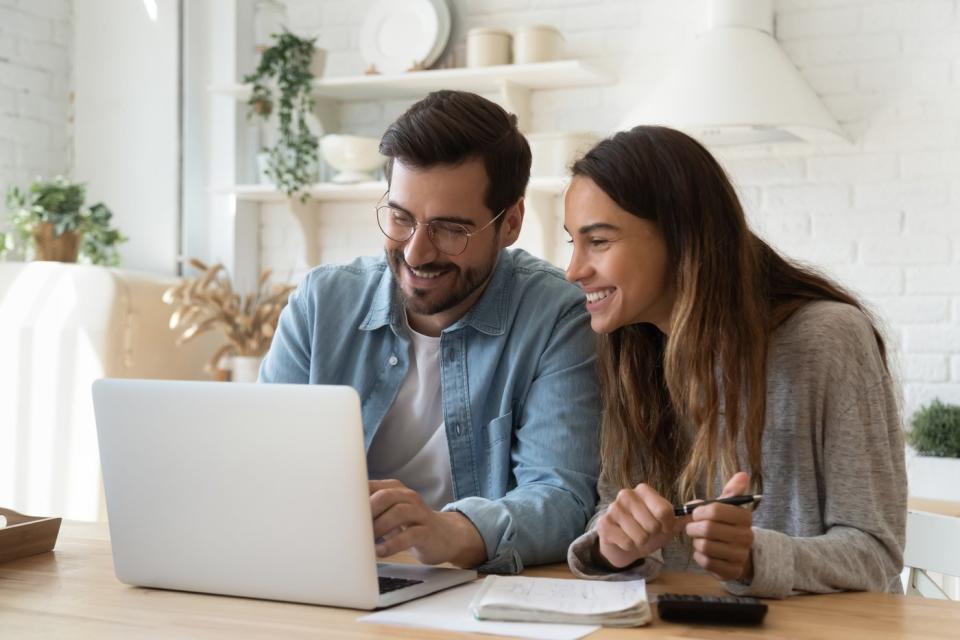 Two investors smile and look at something in a laptop in a living room.