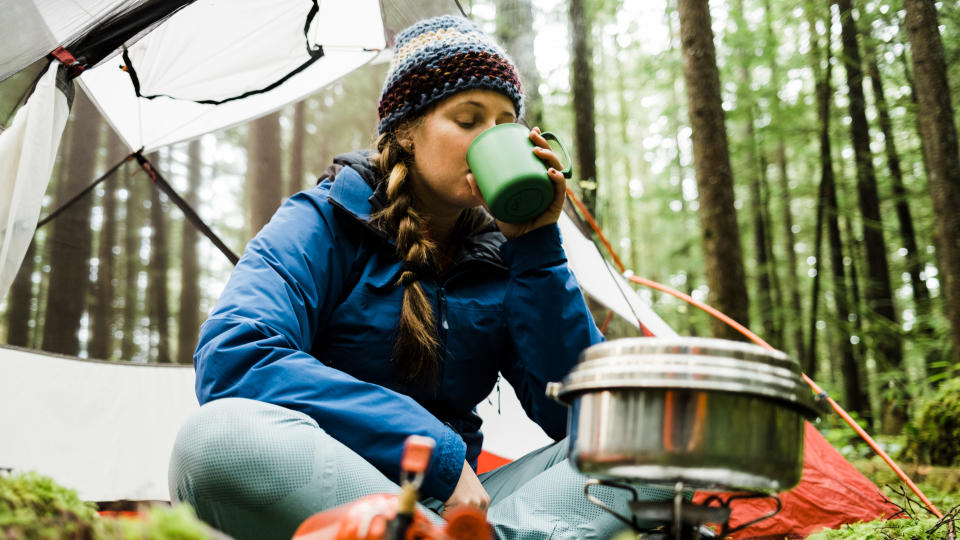 A woman drinking from a mug while camping