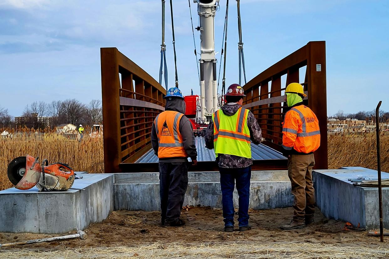 Crews look over the truss bridge installed over the Black River on Tuesday, March 21, 2023, shortly after it was lowered by crane into place. The bridge is part of the larger pathway expected to be installed in time for use by the public later this spring.