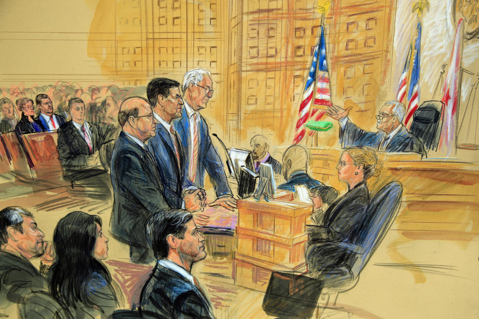 This courtroom sketch depicts former President Donald Trump's former national security adviser Michael Flynn, standing center, flanked by his lawyers, listening to U.S. District Judge Emmet Sullivan, right, as he addresses Flynn and points to the American flag inside the federal court in Washington, Washington, Tuesday, Dec. 18, 2018. Sullivan agreed to postpone Flynn's sentencing so he can continue cooperating with the Russia probe. Flynn's wife Lori Andrade, back left, and son Michael Flynn Jr., with red tie, listen. (Dana Verkouteren via AP)