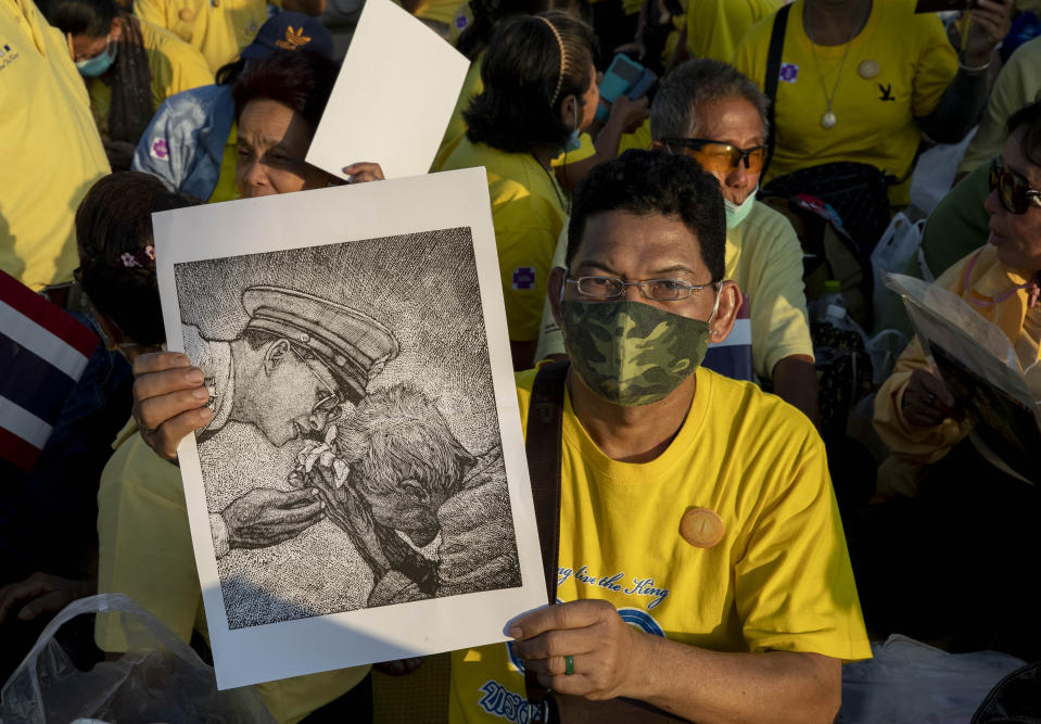 A supporter of Thai monarch displays an image of late King Bhumibol Adulyadej ahead of the arrival of King Maha Vajiralongkorn and Queen Suthida to participate in a candle lighting ceremony to mark birth anniversary of the late king at Sanam Luang ceremonial ground in Bangkok, Thailand, Saturday, Dec. 5, 2020. (AP Photo/Gemunu Amarasinghe)
