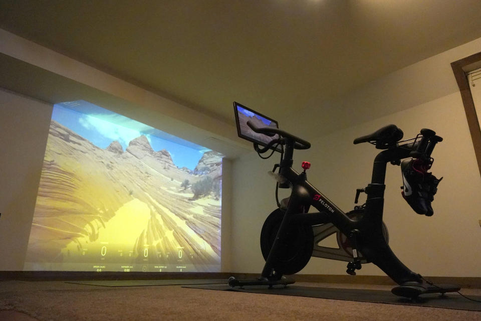 A projection of a desert scene is casted onto a wall near a Peloton fitness bike in a basement home gym, Tuesday, Sept. 15, 2020, in Lutherville-Timonium. Home gyms have picked up in 2020 with sales of exercise bikes going up during the COVID-19 pandemic. (AP Photo/Julio Cortez)