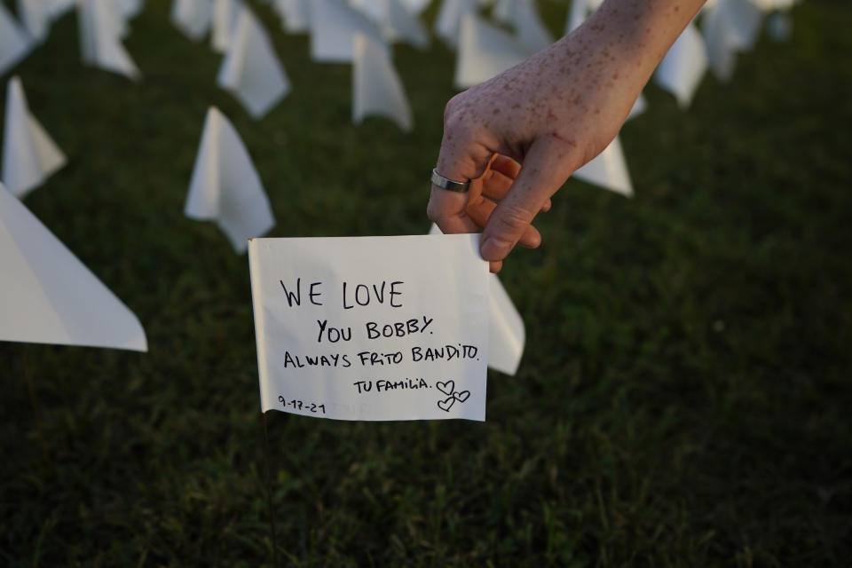 Zoe Nassimoff, of Argentina, holds a white flag that is part of artist Suzanne Brennan Firstenberg's temporary art installation, "In America: Remember," in remembrance of Americans who have died of COVID-19, on the National Mall in Washington, Friday, Sept. 17, 2021. Nassimoff wrote on the flag in memory of her grandparent who lived in Florida and died from COVID-19. (AP Photo/Brynn Anderson)