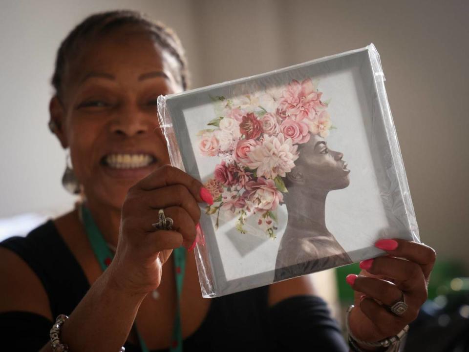 Marie Honoré-Riguad, que ha luchado con problemas de salud mental, sonríe ampliamente después de desempacar un regalo de inauguración de la casa que recibió de un amigo en su nuevo apartamento en el Foot Print to Success Clubhouse, el jueves 6 de junio de 2024, en Pembroke Pines, Florida.