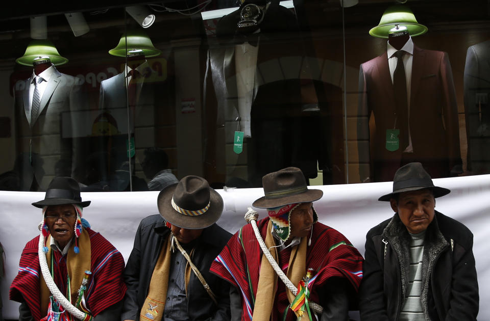 In this Oct. 29, 2019 photo, Aymara supporters of Bolivia's President Evo Morales sit outside the presidential palace, keeping an eye out for anyone who may want to hurt the president, in La Paz, Bolivia. Morales' backers and foes are blocking streets and highways across the country in a dispute over official election results that show the leftist leader winning reelection without a runoff. (AP Photo/Juan Karita)