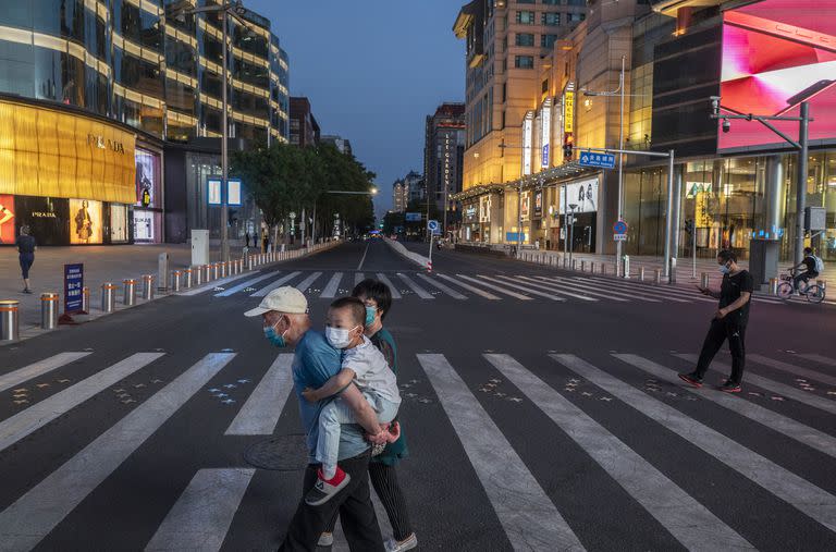 En la ciudad China de Beijing, un hombre cruza a un niño cargado en sus espaldas en una zona comercial.