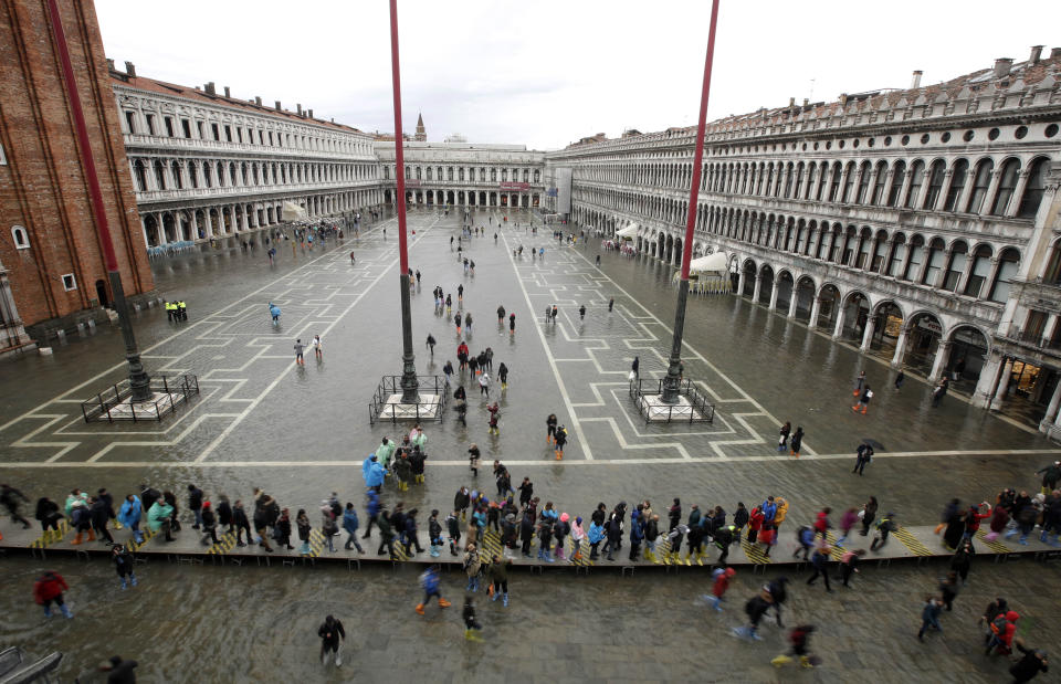 People walk in a flooded St. Mark's Square in Venice, Italy, Tuesday, Nov. 12, 2019. The high tide reached a peak of 127cm (4.1ft) at 10:35am while an even higher level of 140cm(4.6ft) was predicted for later Tuesday evening. (AP Photo/Luca Bruno)