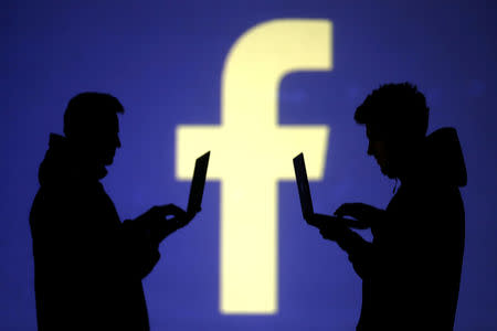 Silhouettes of laptop users are seen next to a screen projection of Facebook logo in this picture illustration taken March 28, 2018. REUTERS/Dado Ruvic/Illustration/Files