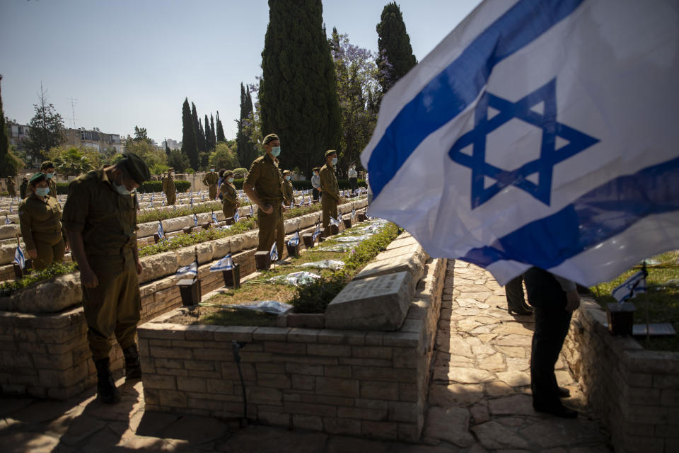 Israeli soldiers wearing protective face masks amid concerns over the country's coronavirus outbreak, wait for a two minute siren marking the annual Memorial Day for fallen soldiers, at a military cemetery in Givataim, Israel, Tuesday, April 28, 2020. This year the government banned public memorial services at military cemeteries as part of its measures to help stop the spread of the coronavirus. Israel marks the annual Memorial Day in remembrance of soldiers who died in the nation's conflicts, beginning at dusk Monday until Tuesday evening. (AP Photo/Oded Balilty)