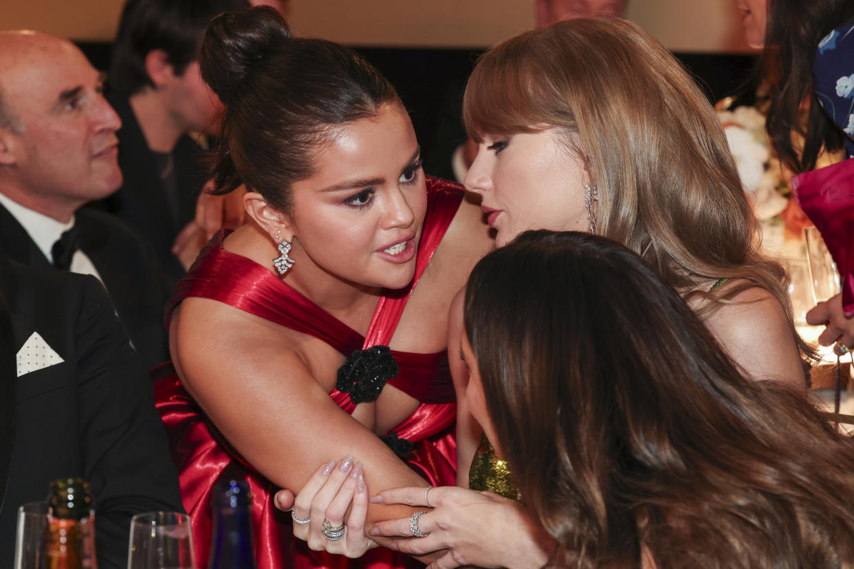 Selena Gomez, leaning in close, talks to Taylor Swift and Keleigh Teller at a table at the Golden Globes.