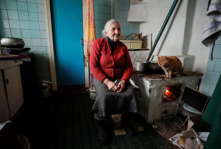 Retired school principal Nadiya Yurchenko, 79, warms herself by a stove as a cat sits nearby in her house in the village of Skryhalivka, Kiev region, Ukraine February 11, 2019. REUTERS/Gleb Garanich
