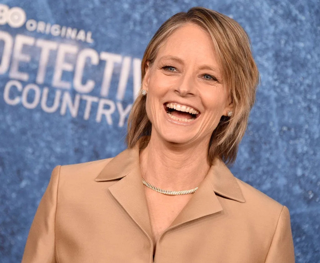 jodie foster smiling in front of a logo for her true detective series