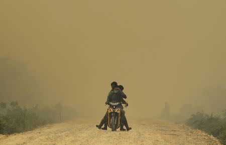 Villagers ride a motorcycle in a haze hit Dumai, in Indonesia's Riau province in this June 21, 2013 file photograph. REUTERS/Beawiharta/Files