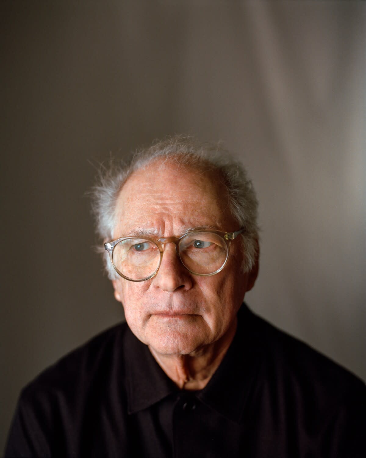 A man with glasses and white hair against a wide background