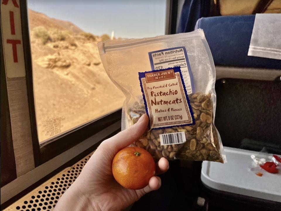 hand holding a bag of nuts and a clementine on an amtrak train