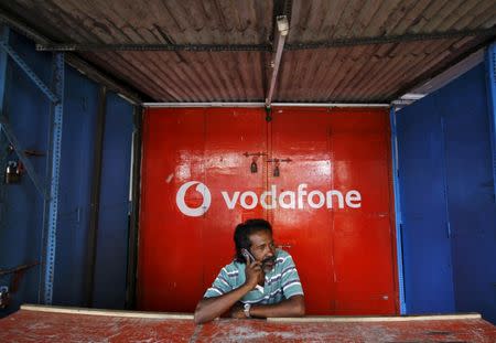 A retail shop owner speaks on his mobile phone outside his closed shop shutters painted with an advertisement for Vodafone at a market in the southern Indian city of Chennai December 30, 2013. REUTERS/Babu/File photo