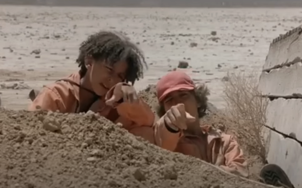 Two characters from the film "Holes" lie on the ground, pointing towards something outside of frame