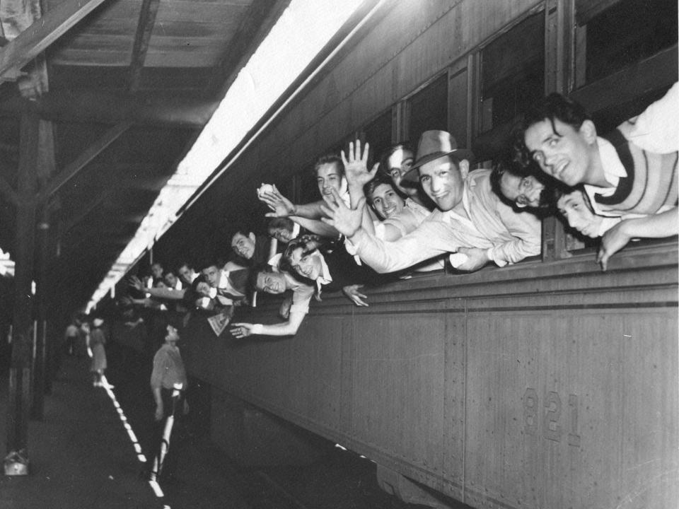 A black and white photo of men leaning out of a train window as it pulls out of the station.