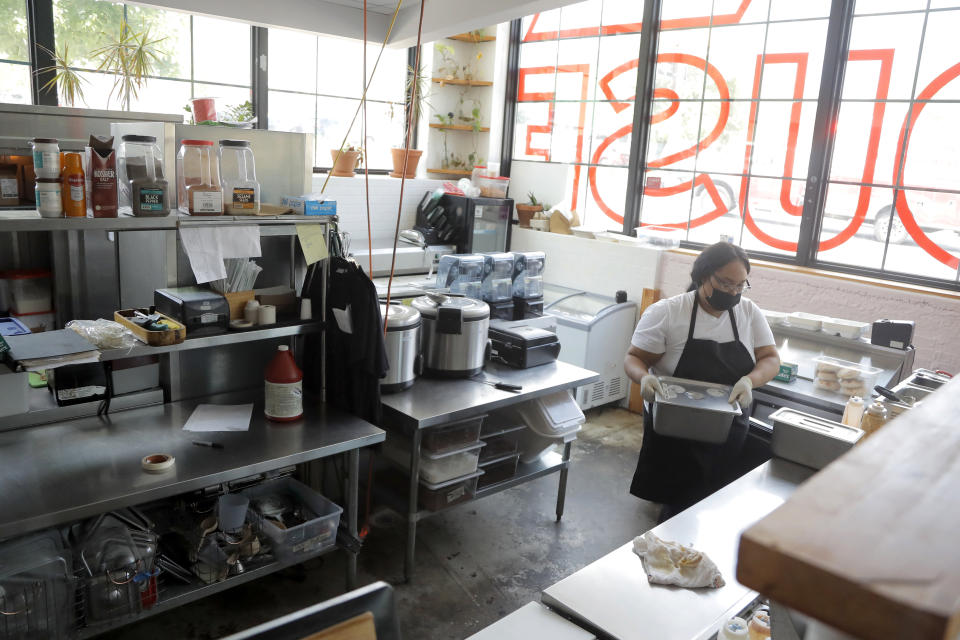 An employee of a food establishment works behind the counter at the R. House food hall, Wednesday, July 15, 2020, in Baltimore. The hall, which houses a variety of restaurants, has modified its seating areas as well as implementing an order and pay by phone system to ensure contactless transactions between restaurant operators and customers. (AP Photo/Julio Cortez)