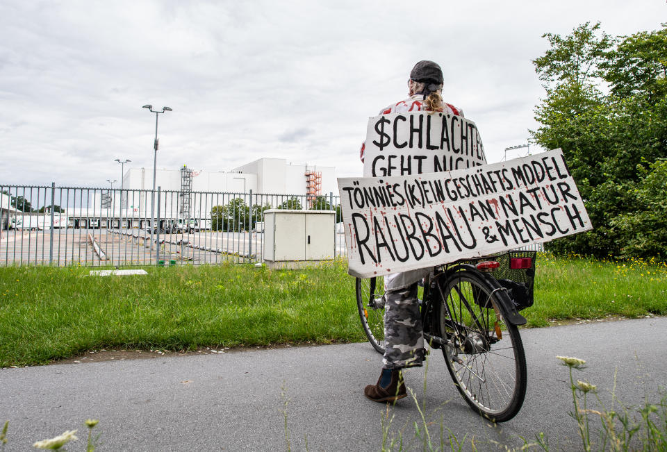 04 July 2020, North Rhine-Westphalia, Rheda-Wiedenbrück: An activist from the "Alliance Together Against the Animal Industry" stands with his bicycle and two banners with the inscription: "$chlachter geht nicht" and Tönnies (k)ein Geschäftsmodell - Raubbau an Natur & Mensch" in front of the Tönnies company complex. Photo: Guido Kirchner/dpa (Photo by Guido Kirchner/picture alliance via Getty Images)