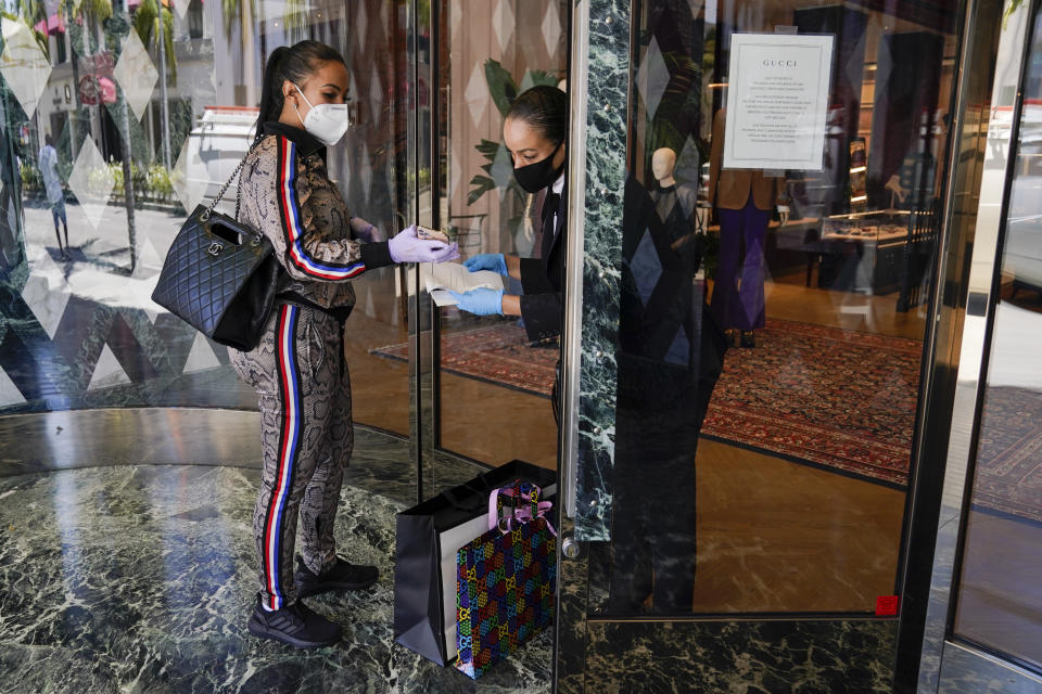Delicia Cordon receives a purchase from a sales person at Gucci on Rodeo Drive Tuesday, May 19, 2020, in Beverly Hills, Calif. The store is closed for in-store shopping, but offers curbside pickup for orders in advance. (AP Photo/Ashley Landis)