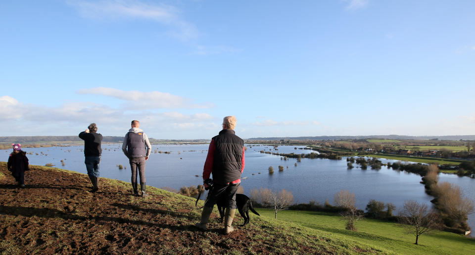 In this photo taken Sunday Feb. 2, 2014, people take photos and look at the flooding from the River Parrett on the Somerset Levels from Barrow Mump, Somerset, England, Here on the Somerset Levels _ a flat, marshy region of farmland dotted with villages and scored by rivers and ditches _ it's often wet. But not this wet. Thousands of acres of this corner of southwest England have been under water for weeks, some villages have been cut off for more than a month, and local people forced to take boats to get to school, work and shops are frustrated and angry. Some blame government budget cuts and environmental bureaucracy. Others point to climate change. Even plump, endangered water voles are the target of ire. (AP Photo/Alastair Grant)