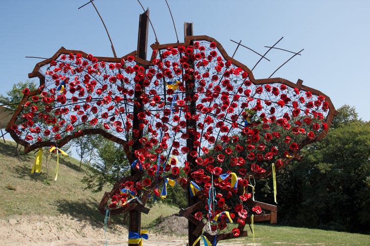 Shape of the territory of Ukraine filled with red poppies, with some blue and yellow ribbons.