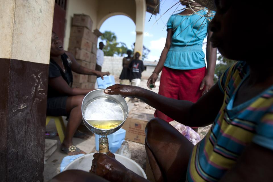 In this Monday, March 24, 2014 photo, an aid worker fills a bottle with cooking oil during distribution of food by the U.N. World Food Program at a local school in Bombardopolis, northwestern Haiti. The agency said it has given food to 164,000 people in the region so far, as well as 6,000 seed kits for farmers. (AP Photo/Dieu Nalio Chery)