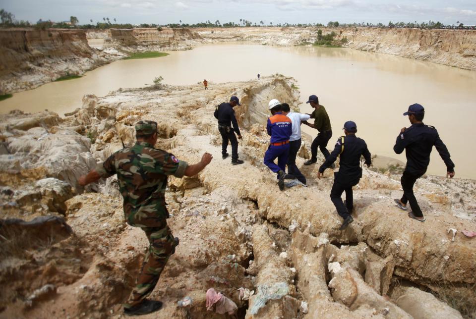 Rescue workers walk at the site where a Cambodian military helicopter crashed on the outskirts of Phnom Penh July 14, 2014. The military helicopter crashed on Monday, killing five and injured one, police told Reuters. A Cambodian air force official said authorities are still investigating the cause of the crash. (REUTERS/Samrang Pring)