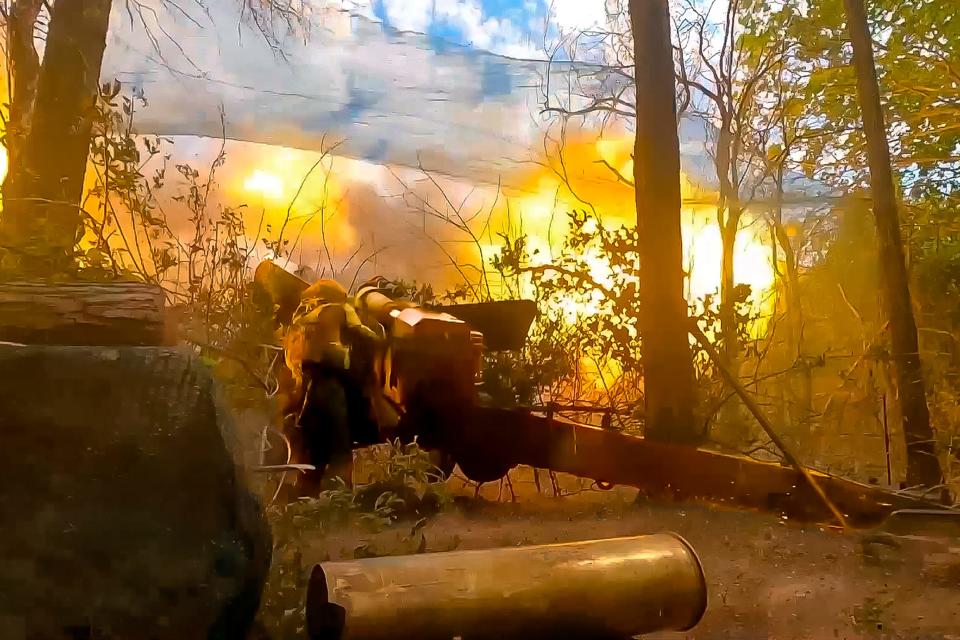 A Russian soldier firing artillery, fire erupting from the barrel.