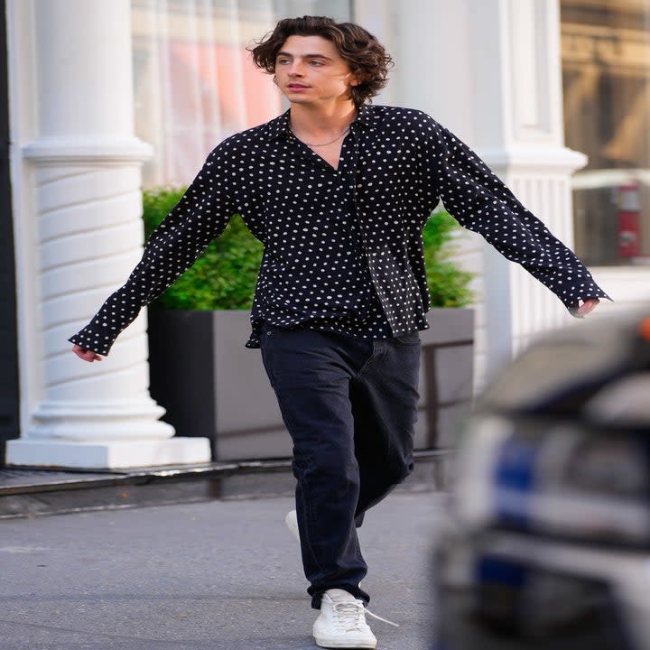 A paparazzi photo of Timothee Chalamet exiting a building wearing a spotted shirt and jeans